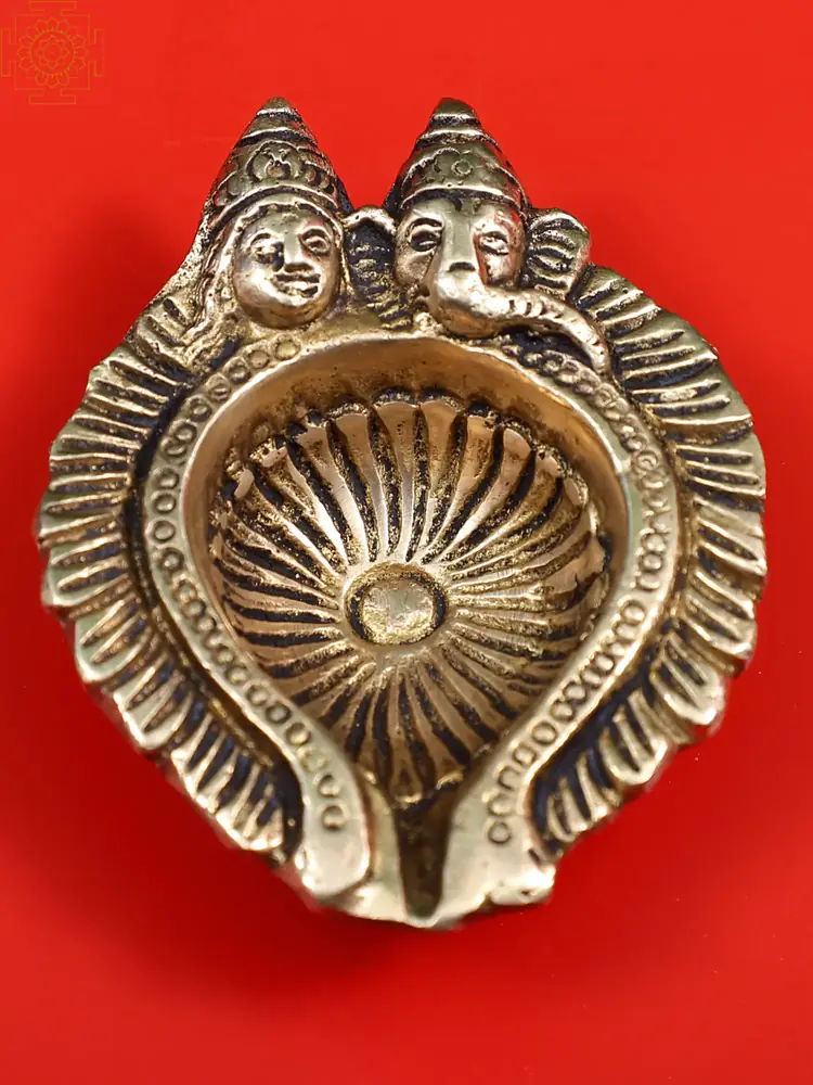 Brass leaf shaped diya with Lakshmi and Ganesha figures on a red ground