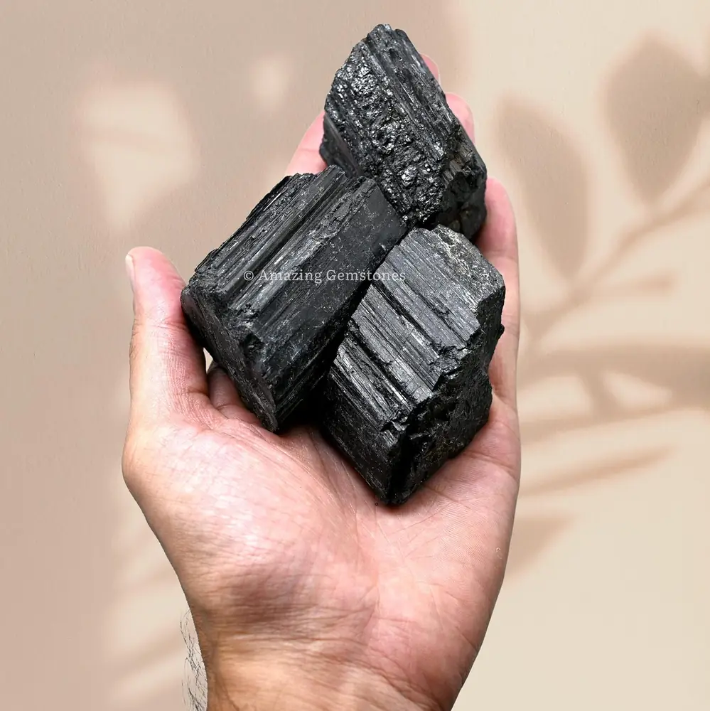A hand holding black tourmaline pieces to show their size
