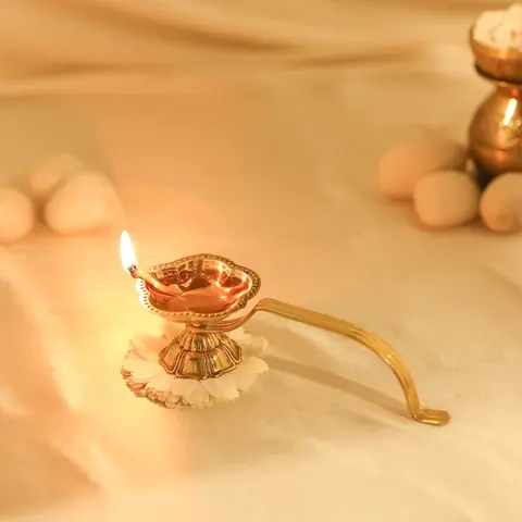 Lit brass aarti diya with a flame on a cream cloth