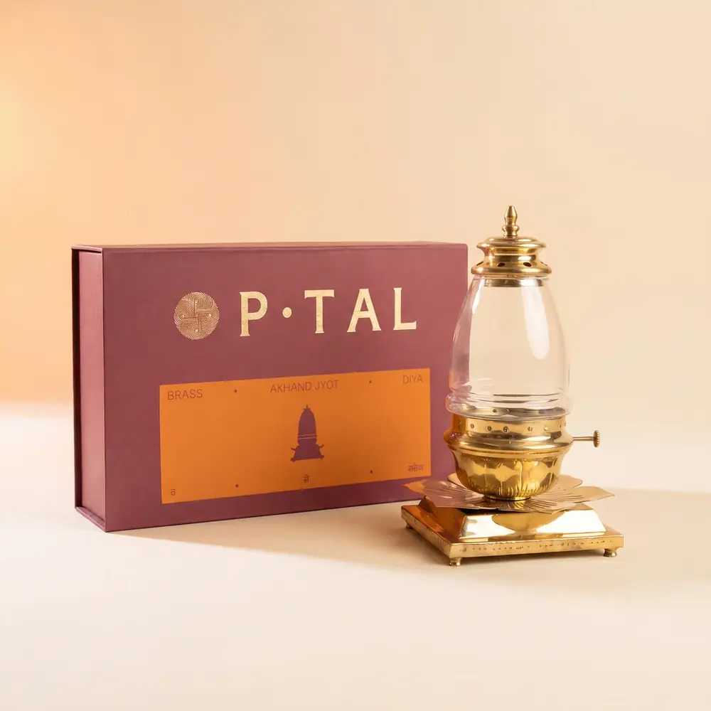 Brass akhand jyot diya with glass chimney beside its box