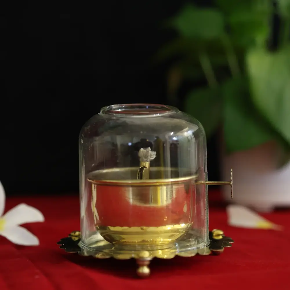 Small brass oil diya under a glass dome on red cloth
