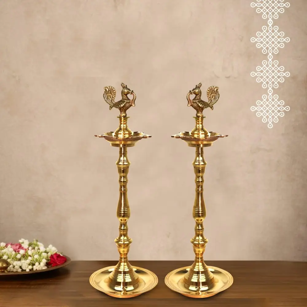 Two brass Annam Kuthu Vilakku lamps beside flowers on a wooden table