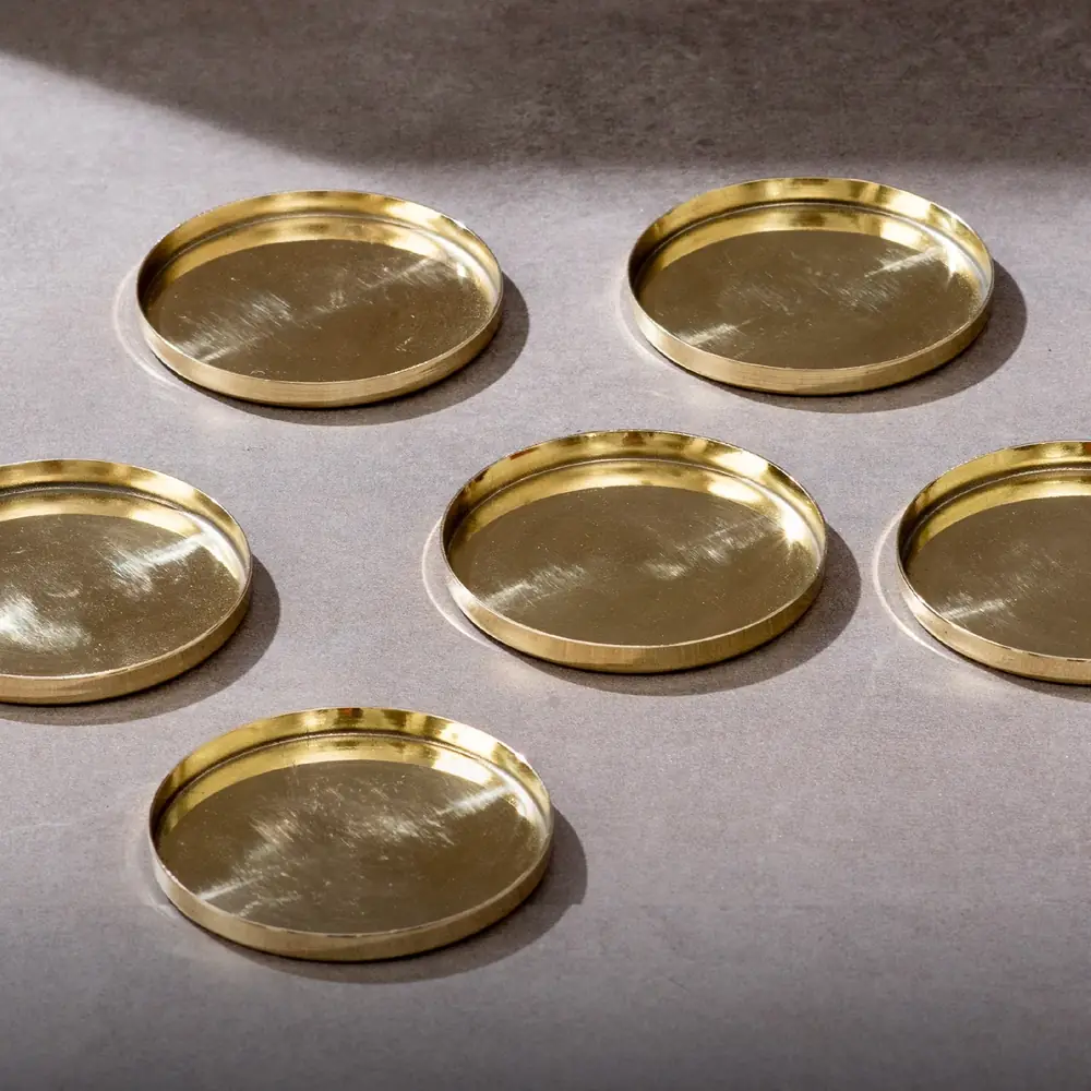 Six brass coasters spread on a grey ground