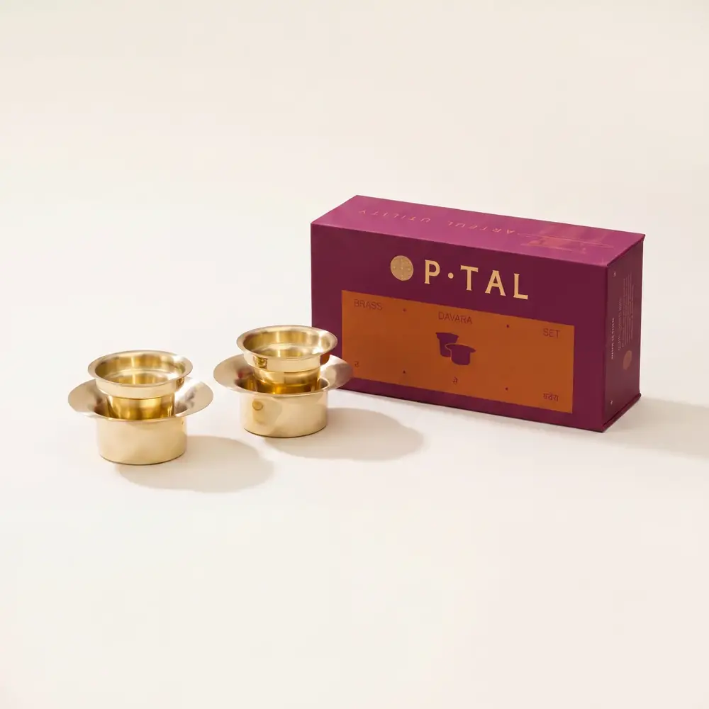 Two brass davara sets next to a maroon gift box