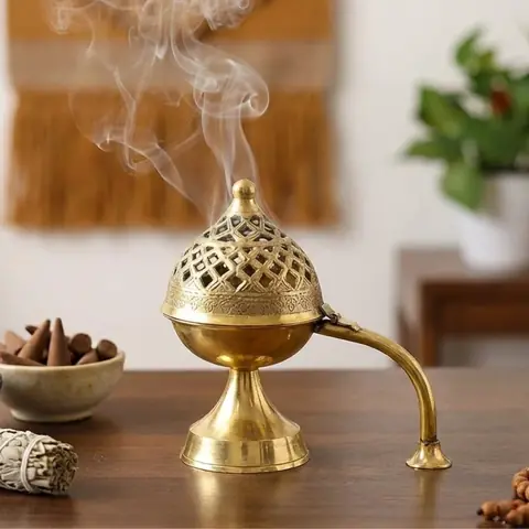 The dhoop daan with smoke rising, beside incense and a plant