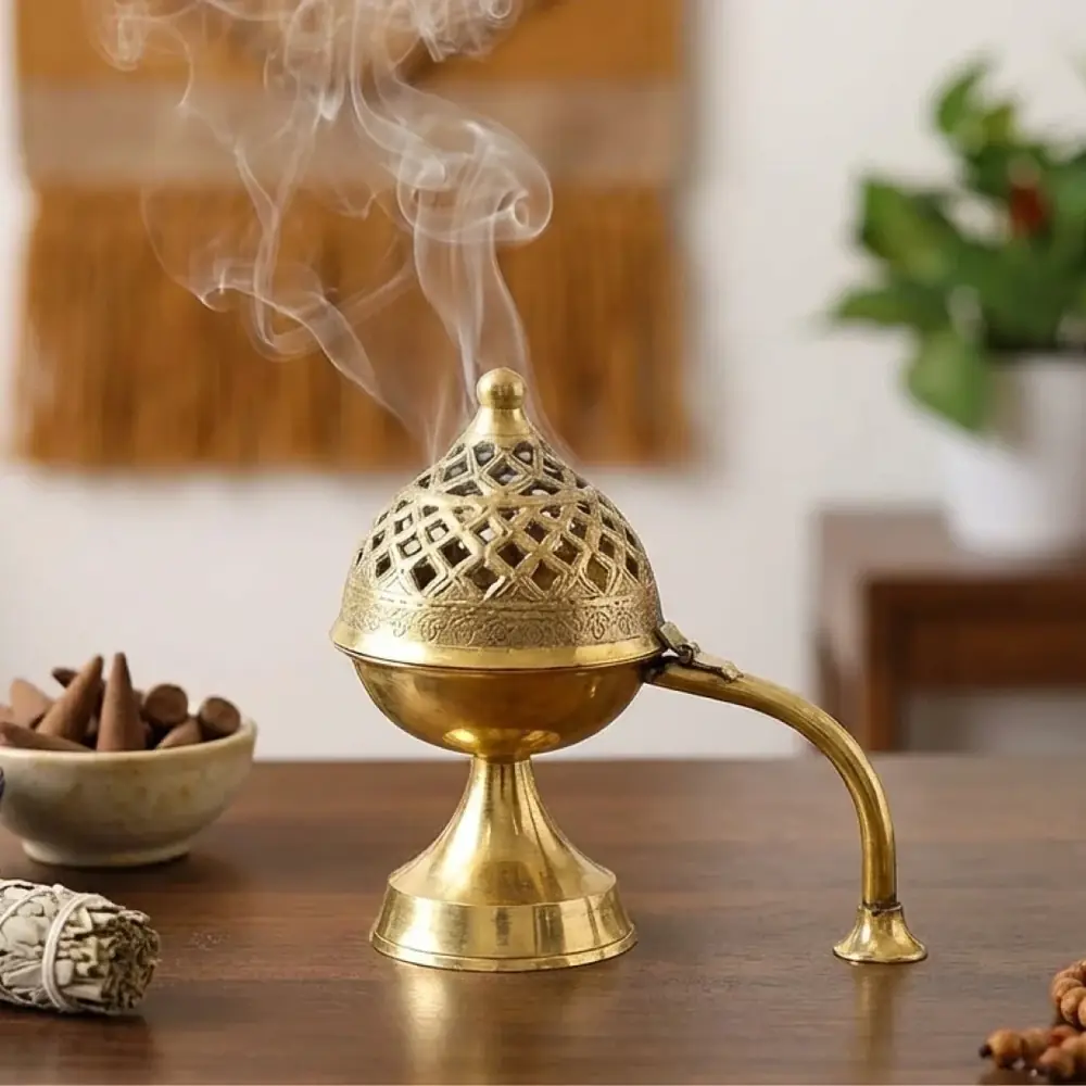 The dhoop daan with smoke rising, beside incense and a plant