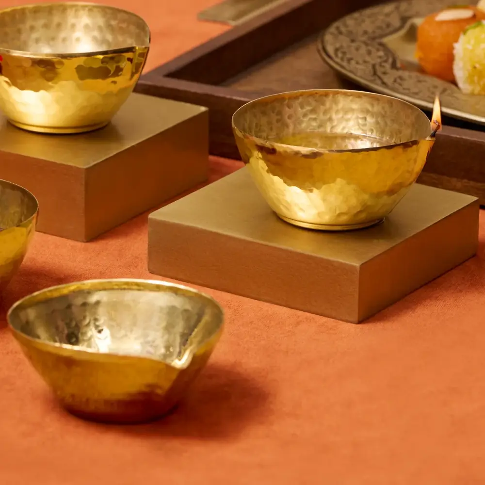 Hand-hammered golden brass diya bowls on a gold stand