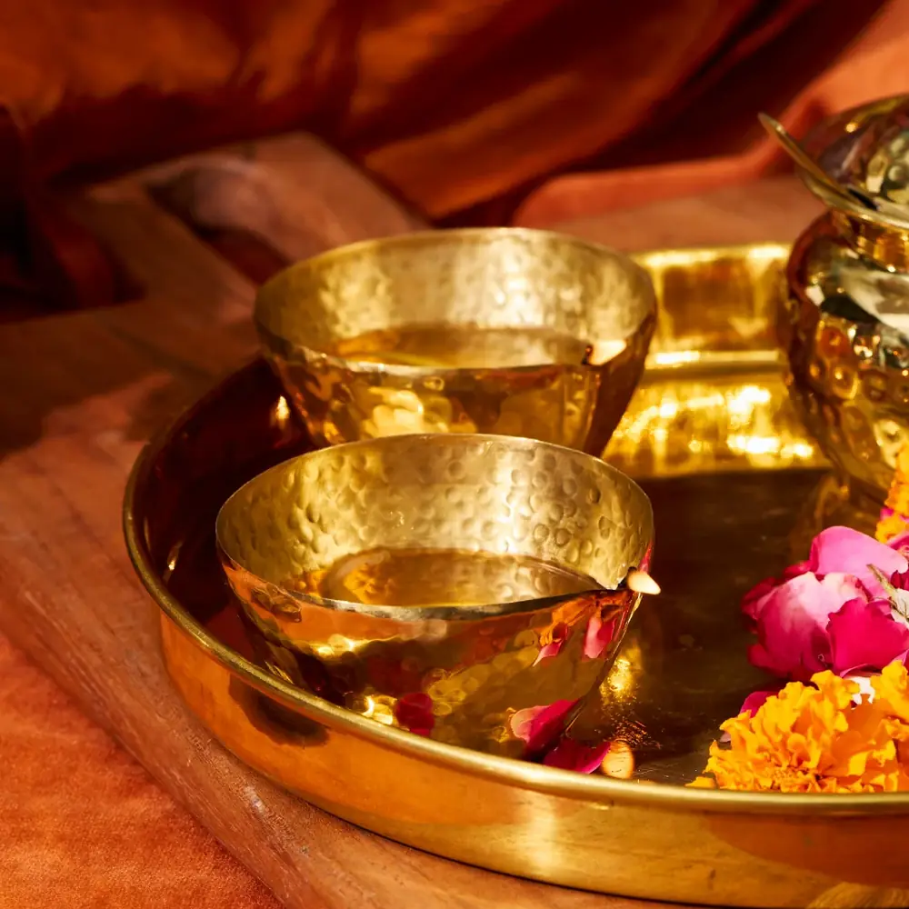 Brass diyas in a tray with flowers and a lit flame