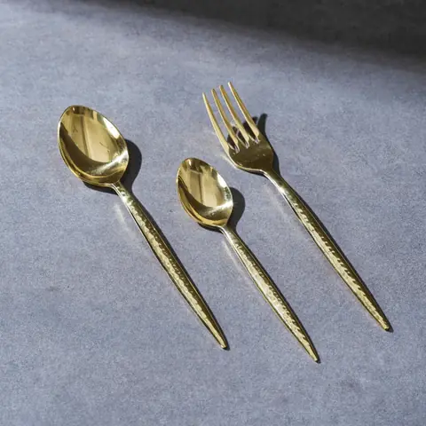 Brass spoon, fork and dessert spoon on a blue grey ground