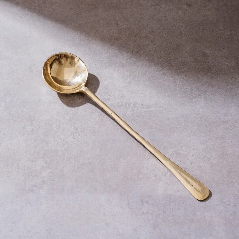 Brass karchi with a round scoop on a grey ground