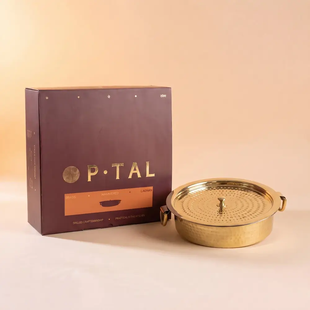 Brass lagaan next to a gift box on a cream ground