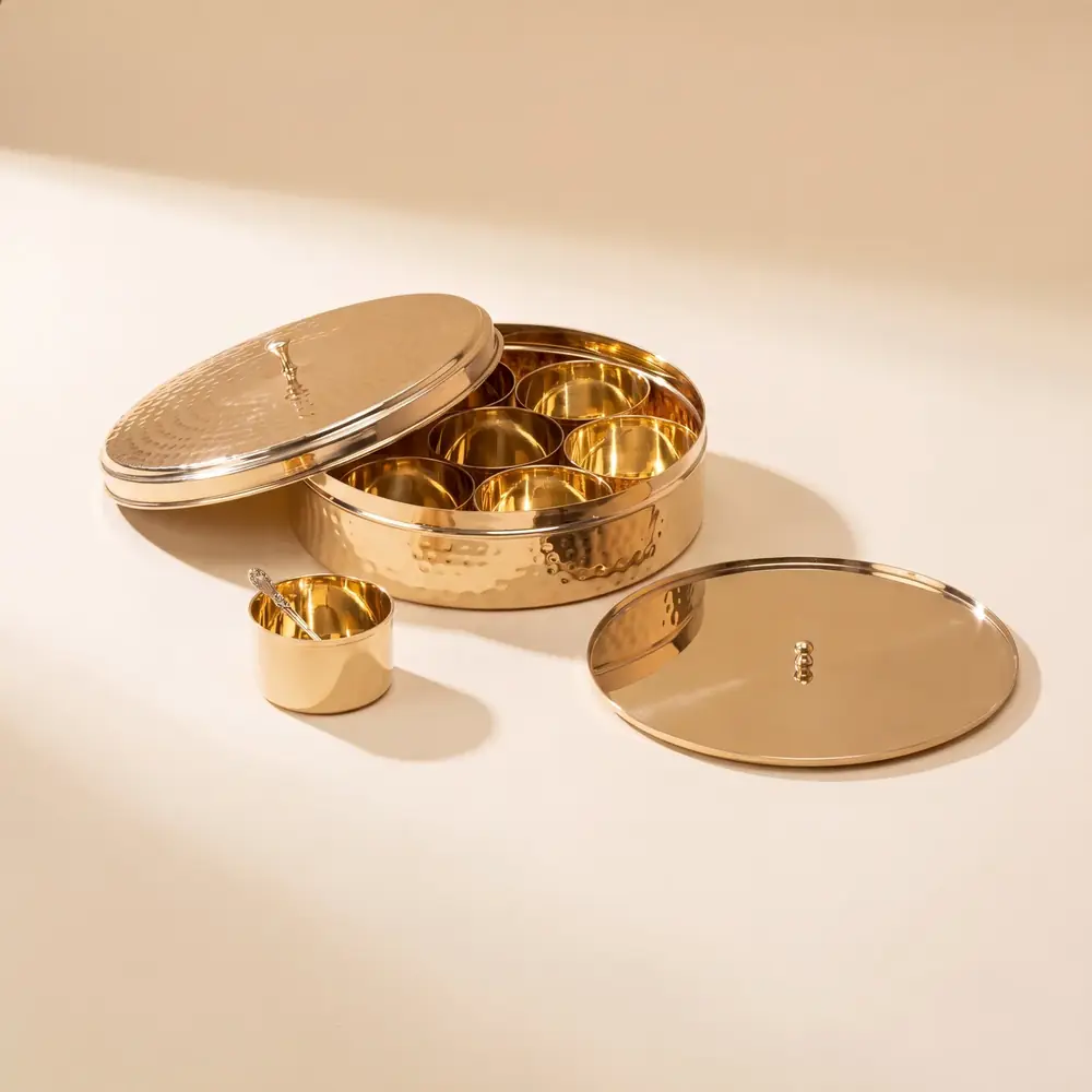 Open brass masala daani with seven bowls and a lid beside it