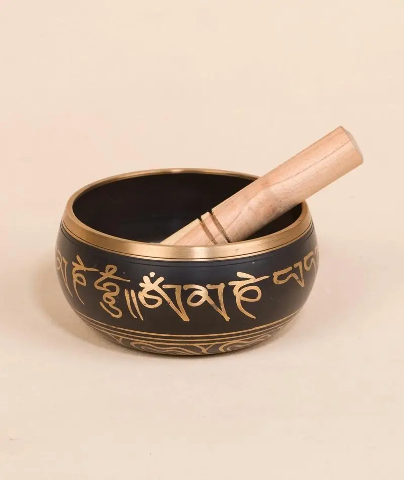 Black and gold singing bowl with its wooden stick beside a lamp