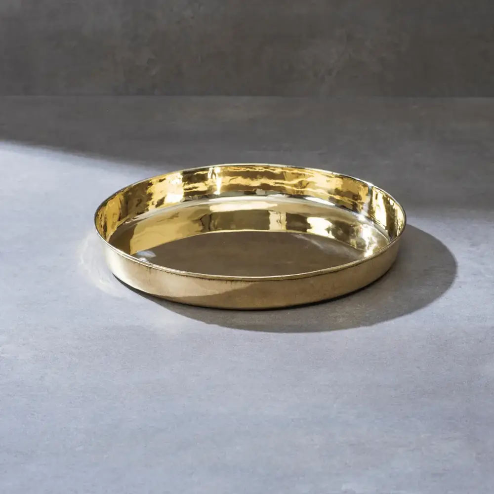 Plain golden brass thaali with a raised rim on a grey surface