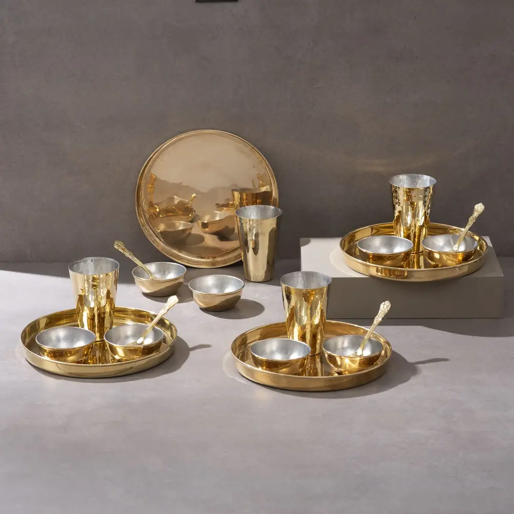 Full brass set of four plates with bowls, glasses and spoons on a grey ground