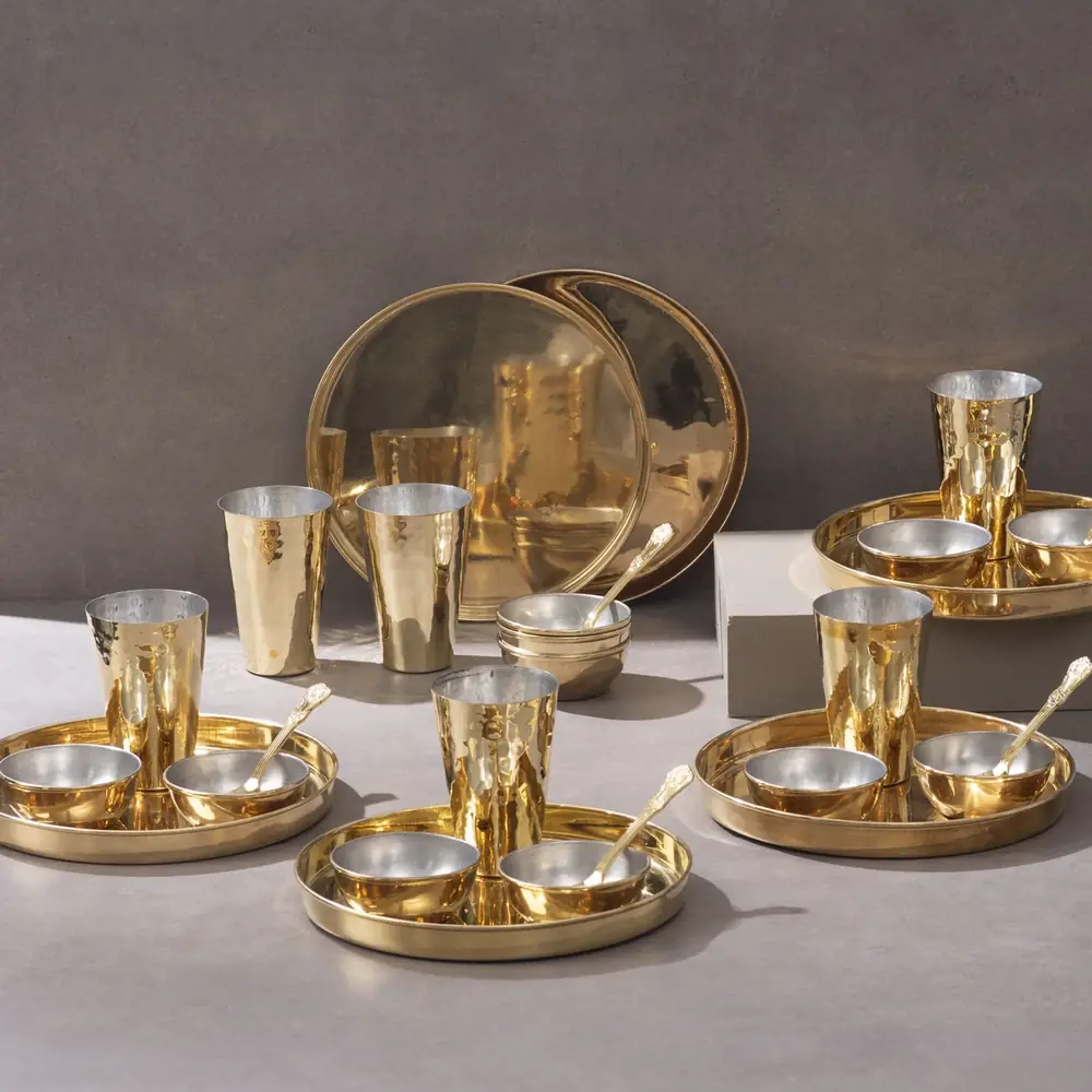 The full 30 piece brass thaali set arranged on a grey ground