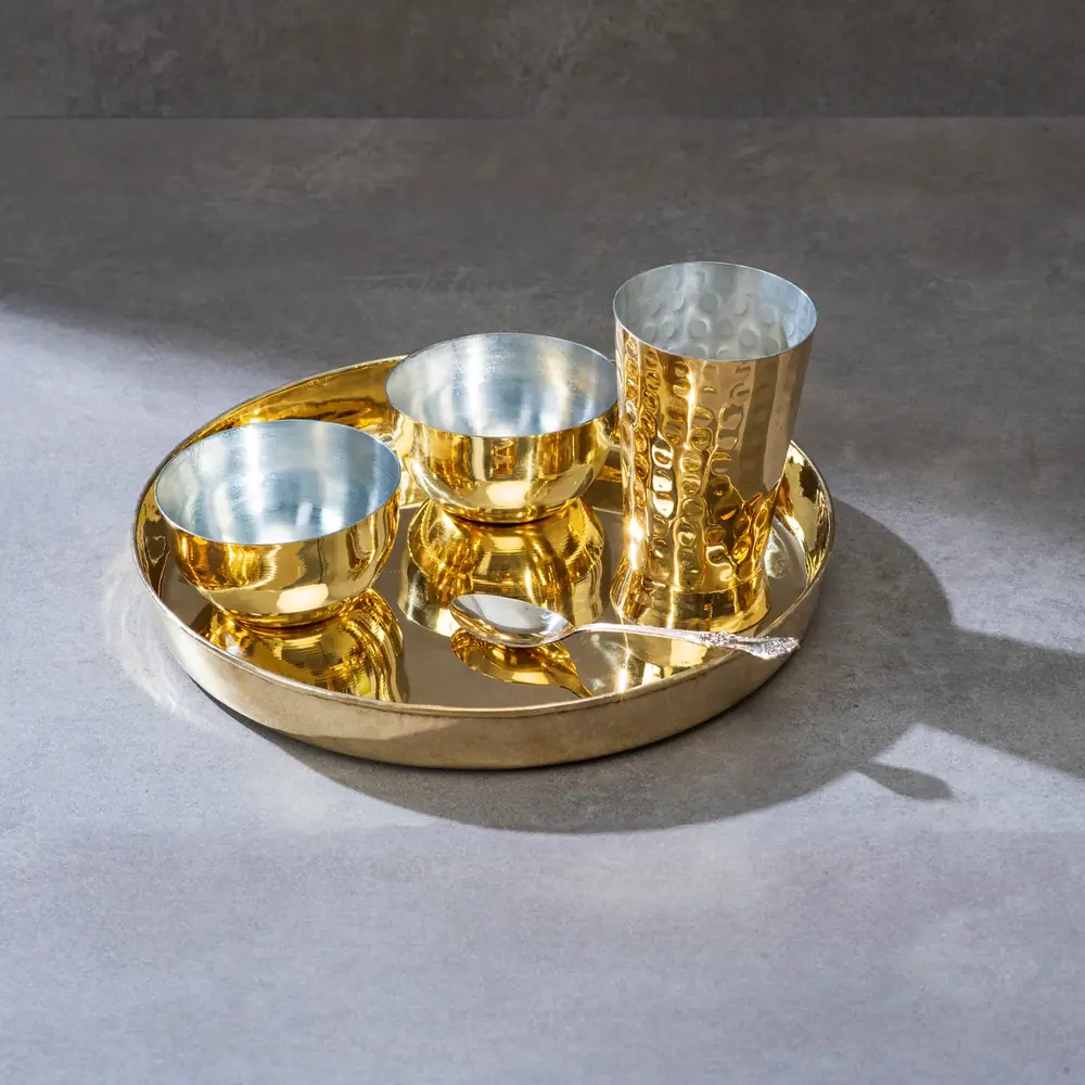 A brass thaali with tin lined bowls and a glass seen from above