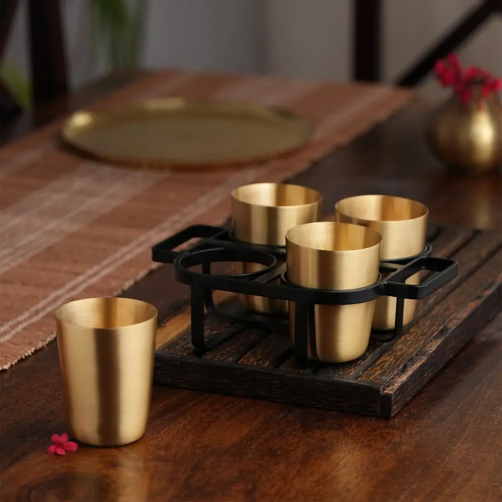 Four brass tumblers in a black iron stand on a wooden table with a runner