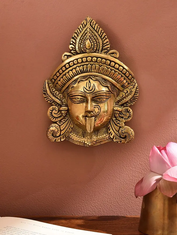 Brass goddess face wall hanging on a rust-red wall