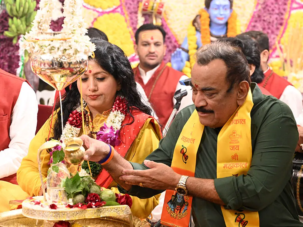Two devotees pouring an offering over a deity image, with priests beside them