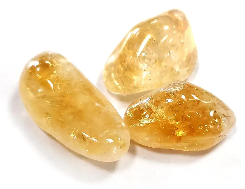 Three tumbled yellow-orange citrine stones on a white ground