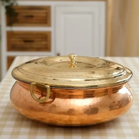 Copper handi with a brass handle on a checked cloth