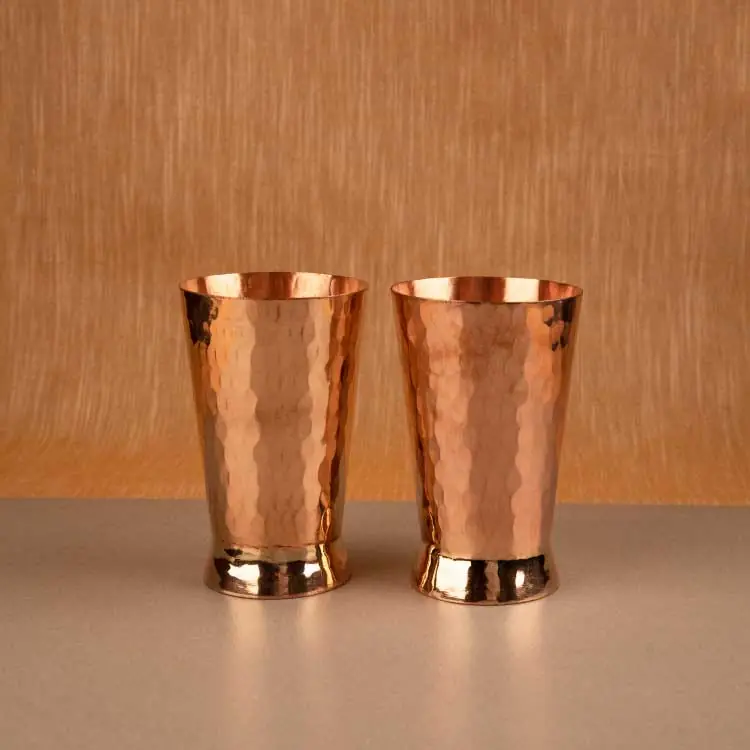 Two hammered copper glasses side by side on a tan ground