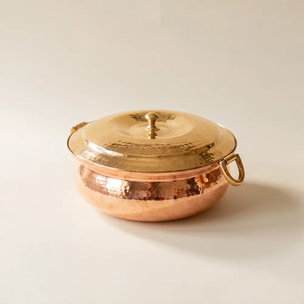 Hammered copper lagan with a golden lid on a plain pale ground