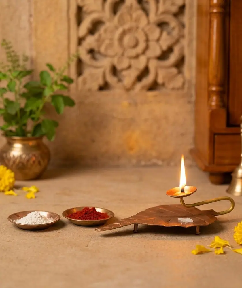 Copper peepal leaf holder with a lit flame in a small puja corner
