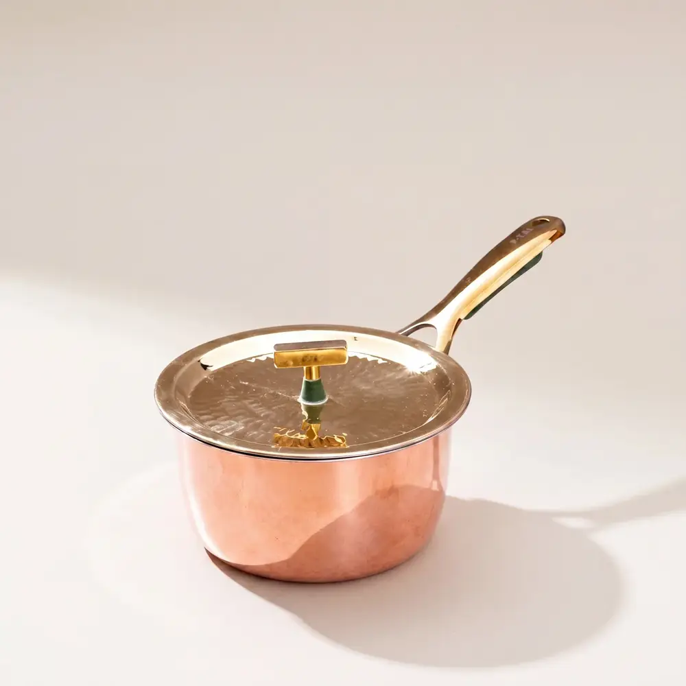 Copper saucepan with a lid and a long handle on a pale ground