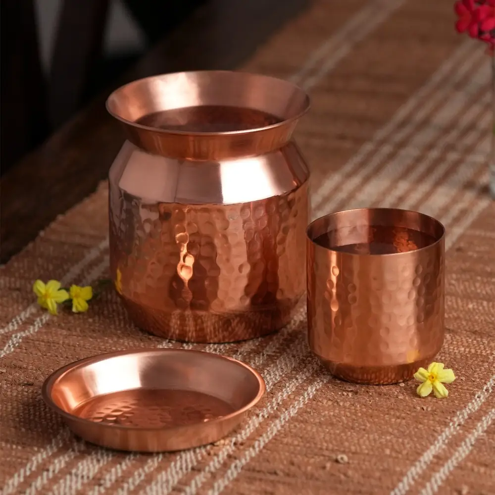 Hammered copper sombu with a tumbler and a round lid on a woven cloth