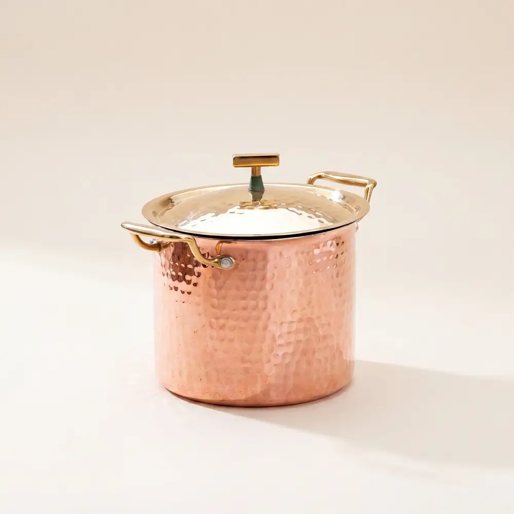 Hammered copper stockpot with a lid on a white ground