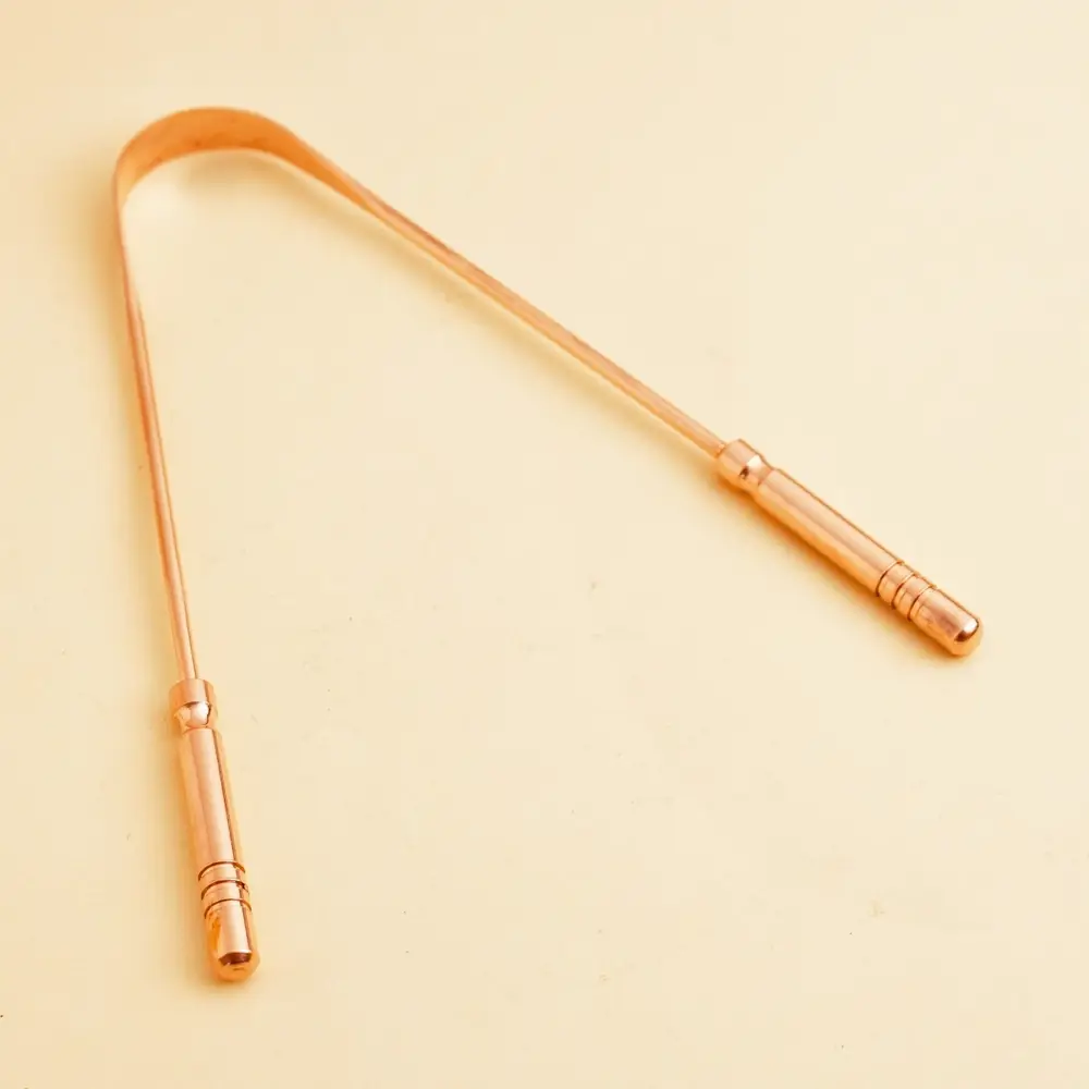 Copper tongue cleaner on a cream ground