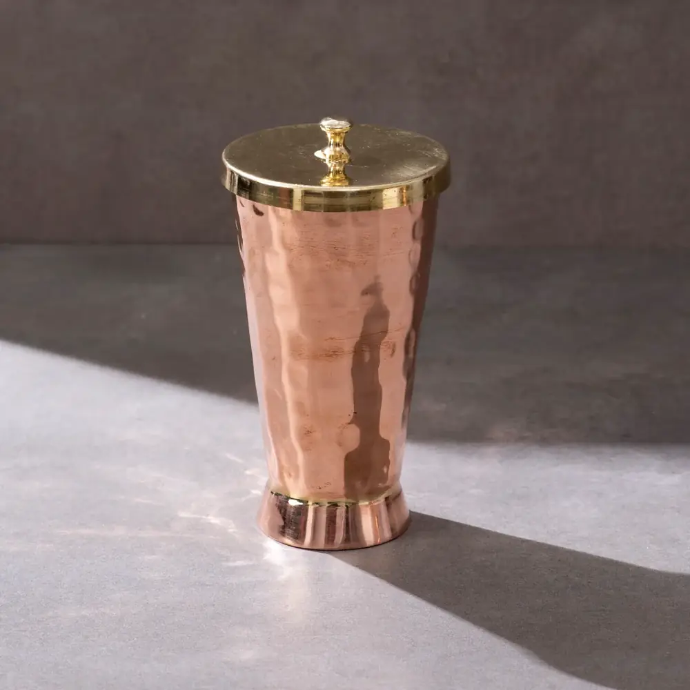 Copper tumbler with a brass lid on a plain grey ground
