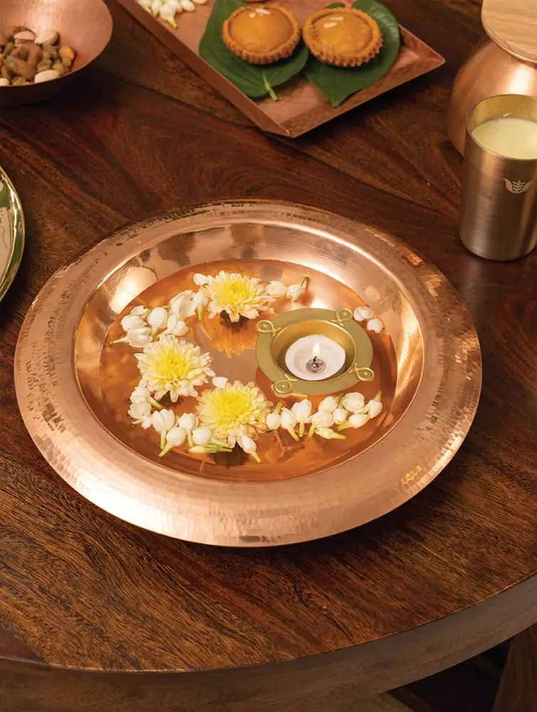 Copper urli with flowers and a lamp on a wooden table
