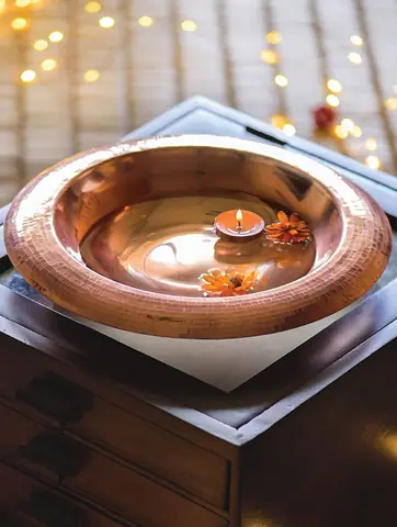 Copper urli with a lit lamp and warm lights behind