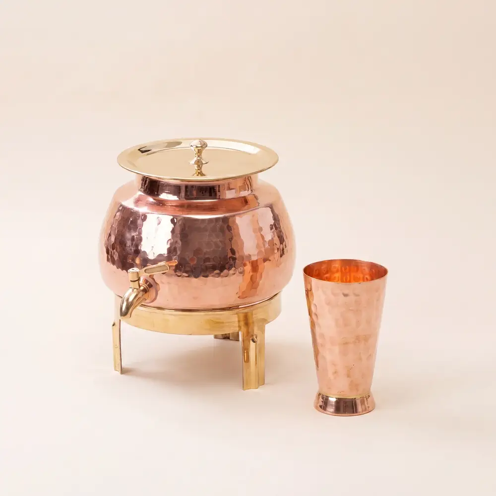 Copper dispenser on a gold stand with a copper glass beside it