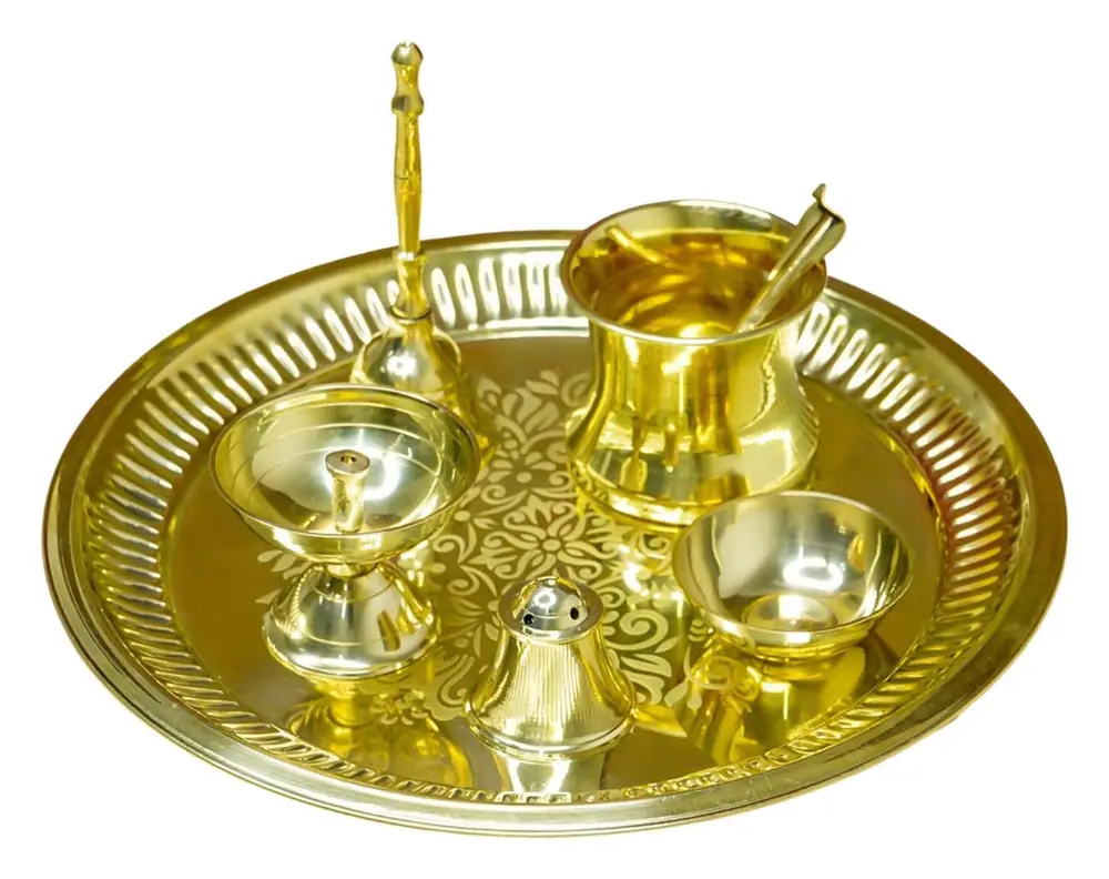 Brass pooja thali set with bell, lamps and cups on a plain white ground