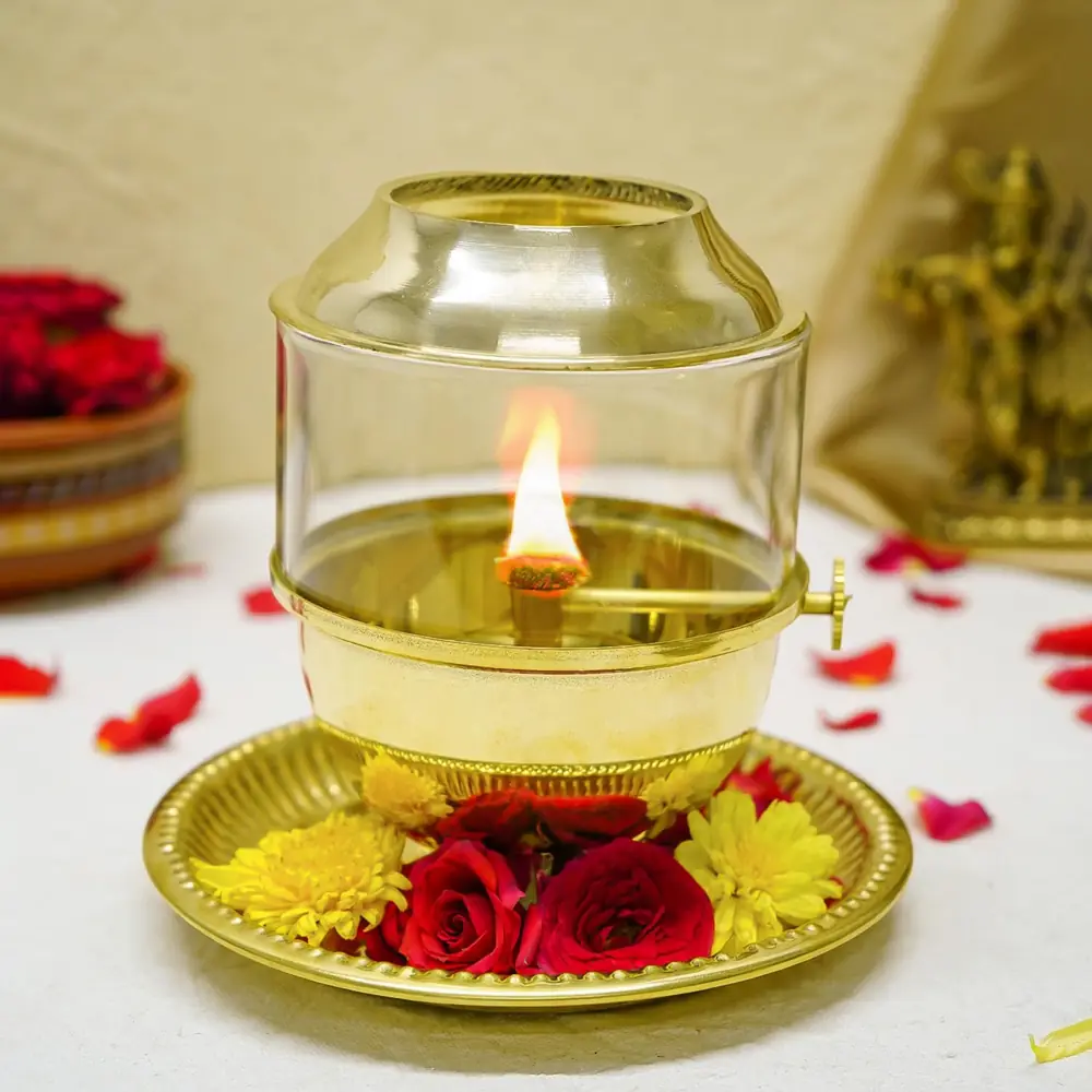 Lit brass Akhand Jyot diya with glass cover on a brass plate with red flowers