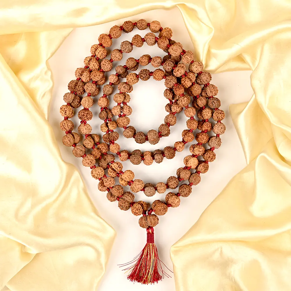 Rudraksha mala coiled on pale yellow cloth with a red tassel