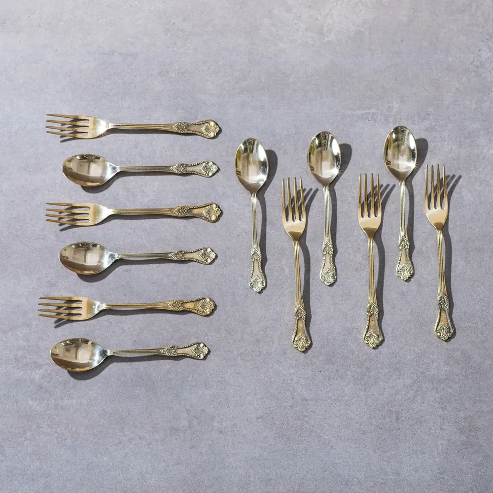 Six forks and six spoons of engraved brass laid out on a grey ground