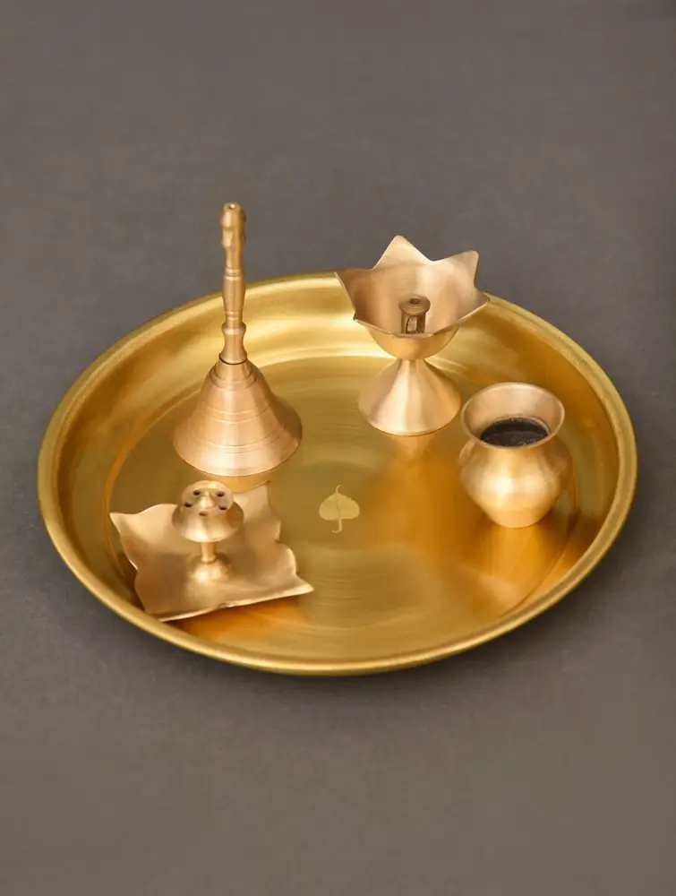 Golden brass thali with a bell, lamp and small pieces on a grey ground