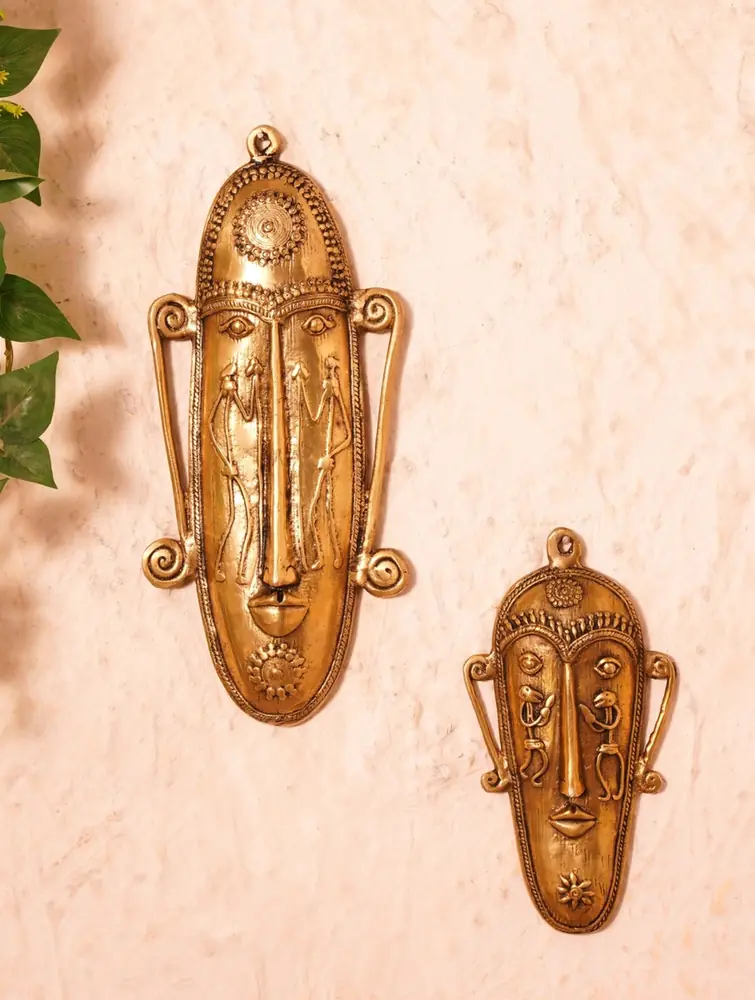 Two brass face masks of different sizes on a pale wall