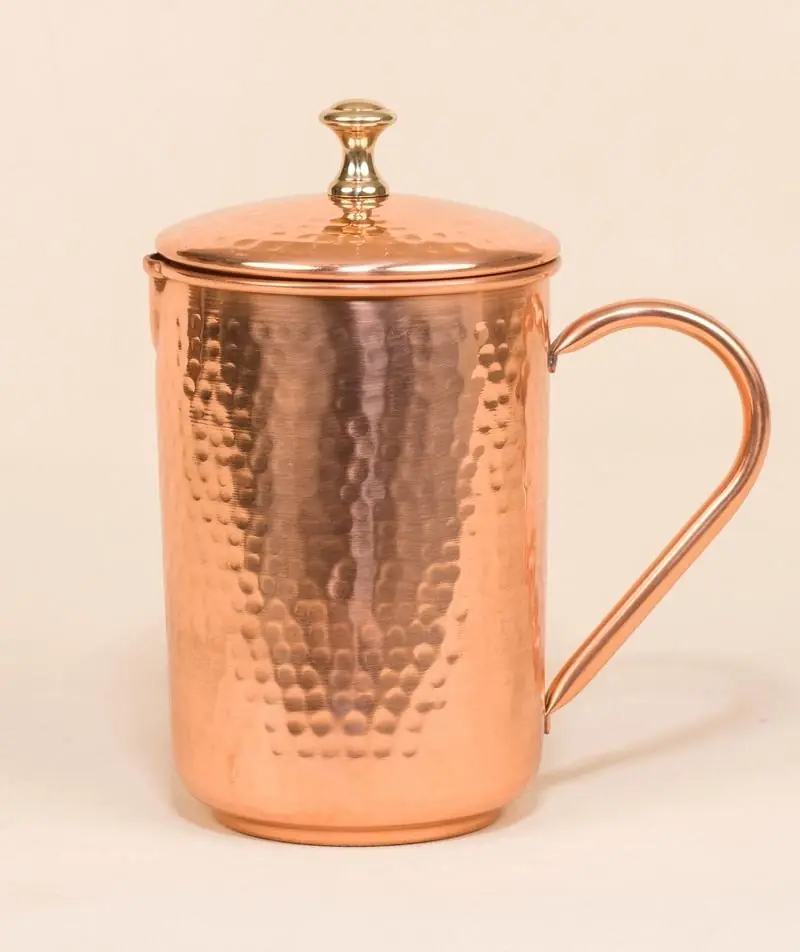 Hammered copper jug with its lid on a plain ground