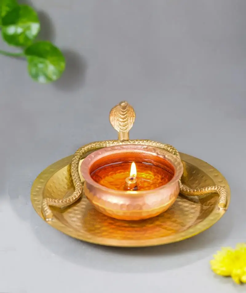 Lit lamp with cobras around the bowl on a gold tray