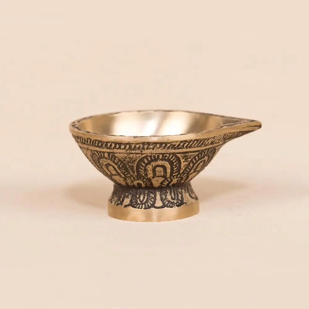 Brass diya with carved sides on a pale ground