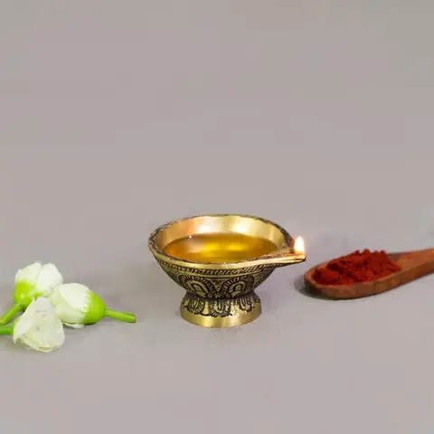 Brass diya filled with oil on a grey ground with a flower