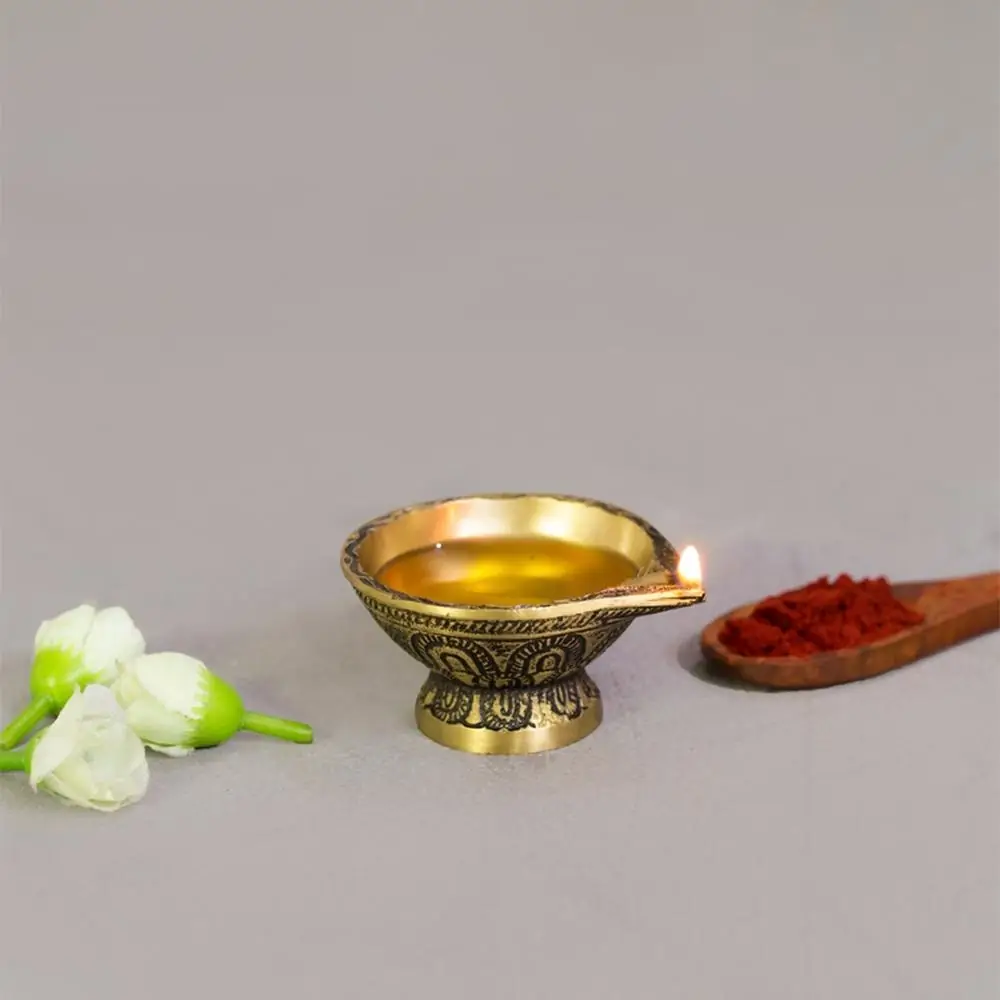 Brass diya filled with oil on a grey ground with a flower