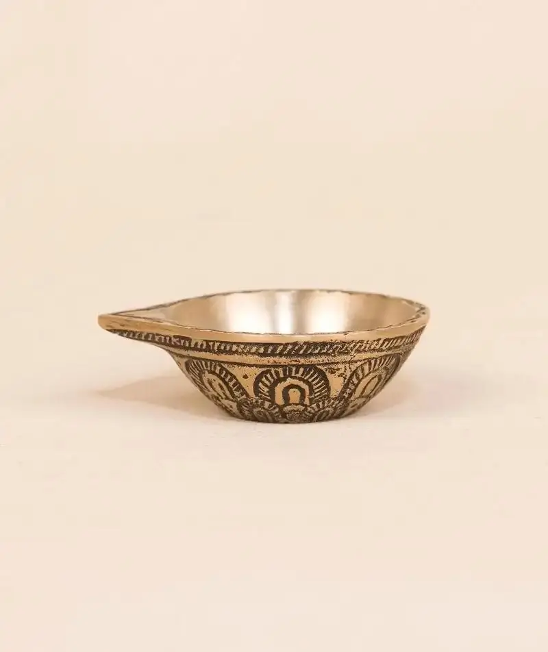 Small antique brass diya beside flowers and kumkum