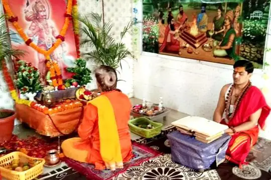 Priests performing a ritual in a room with a Hanuman picture